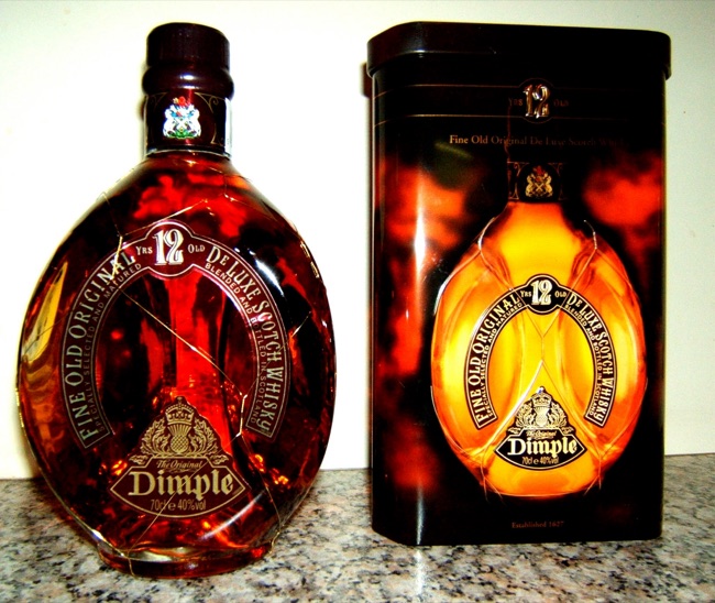 Dimple whisky in a low broad pinched triangular glass flask wrapped in fine wire, standing beside its matching presentation carton.