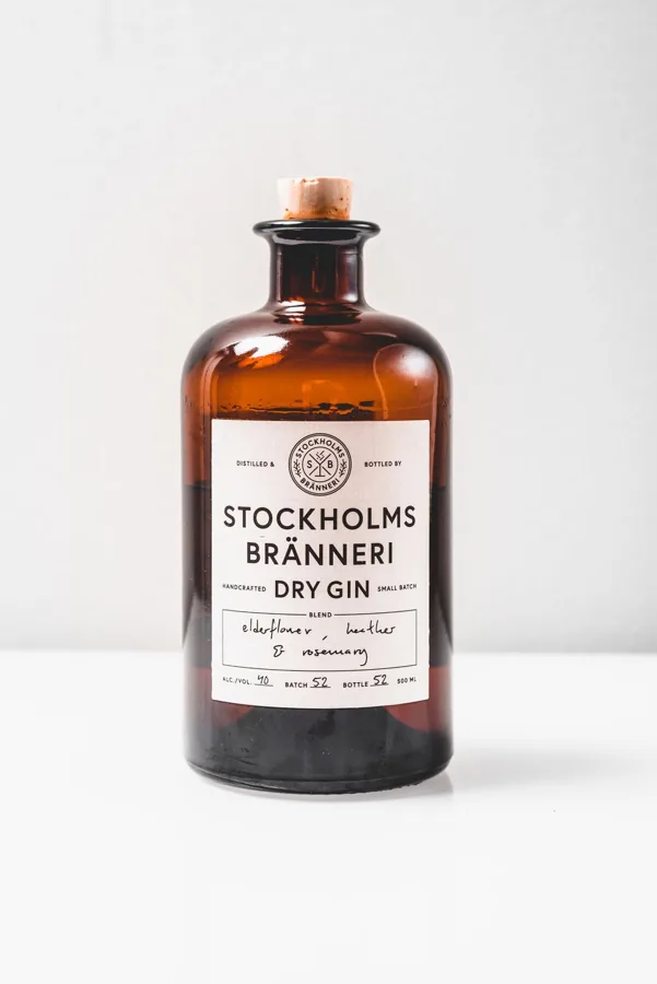 Single squat amber Stockholms Bränneri gin bottle on bright neutral background, broad round shoulders and natural cork.