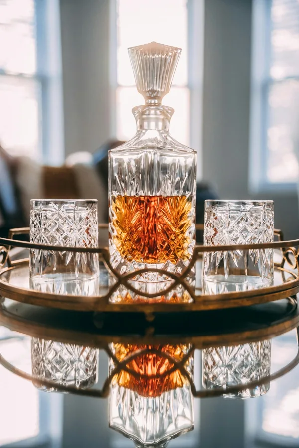 Unbranded tall cut-glass whisky decanter with faceted stopper, two tumblers and brass tray.
